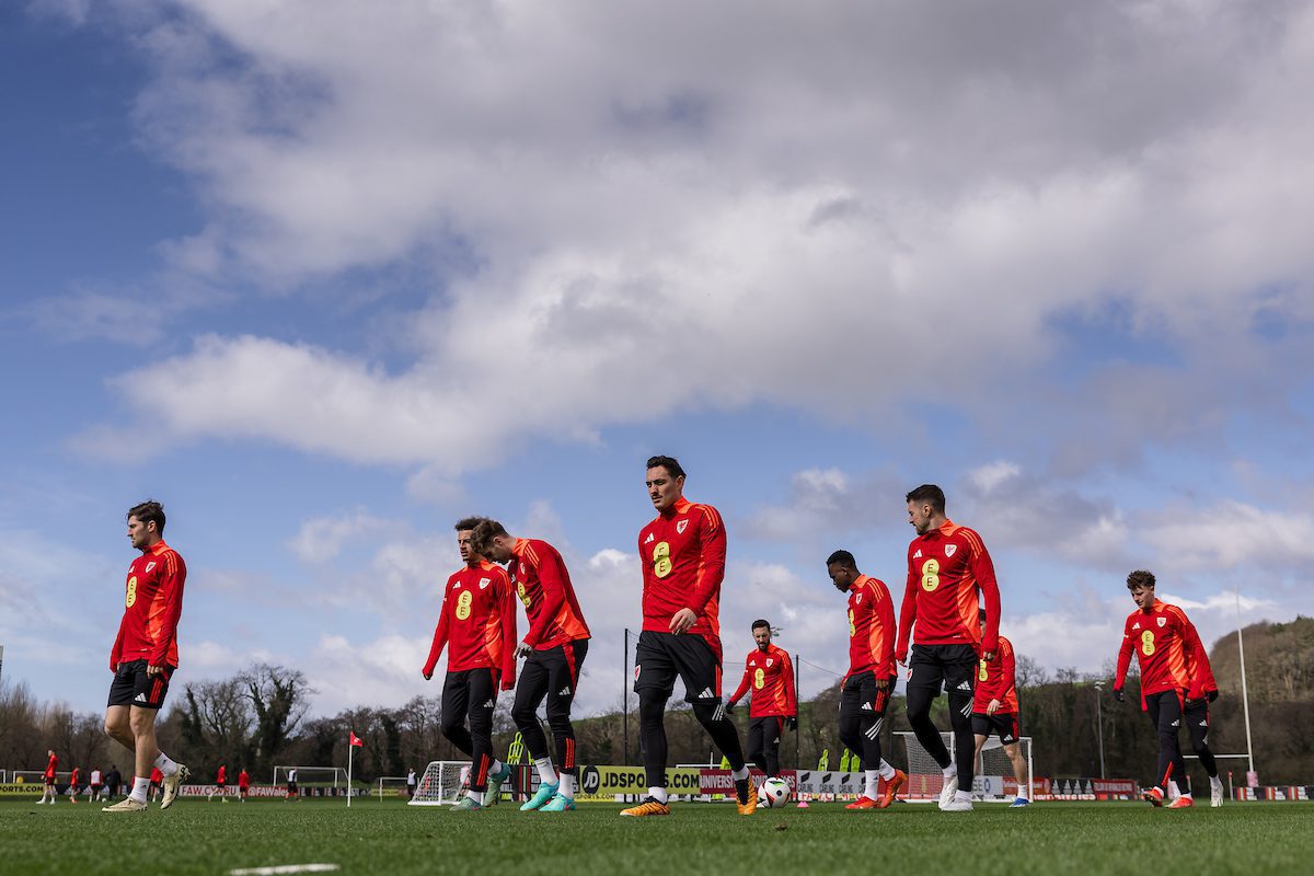 A soccer team in red uniforms trains on a green field under a cloudy sky.