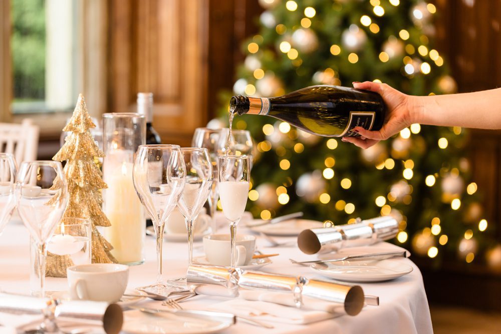 A hand pours champagne into a flute on a festive table, perfect for celebrating Christmas holiday 2026.